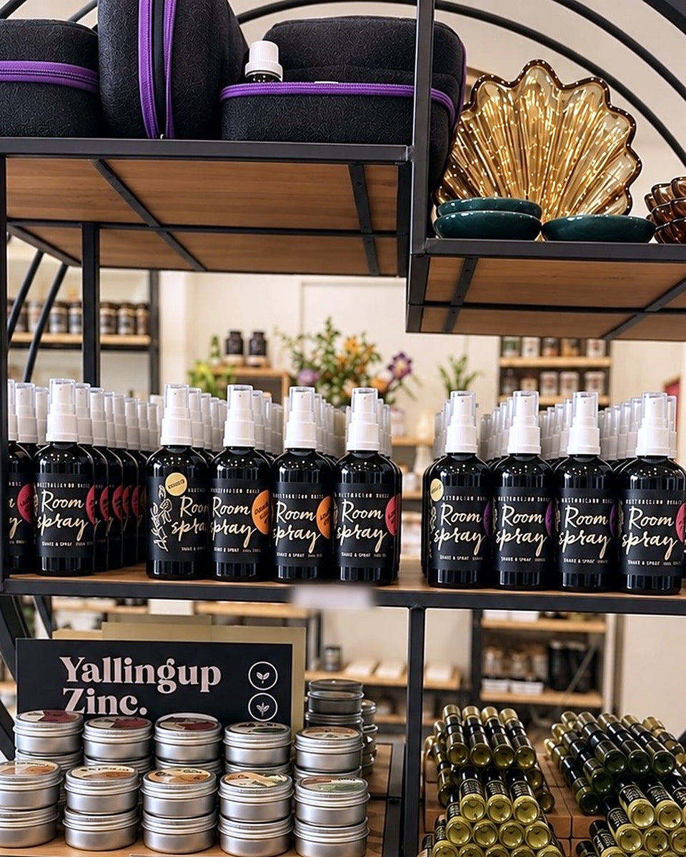 Shelves of black Corrynne's room spray bottles, small round tins and roll-on bottles on a round metal display in the shop in Dunsborough.