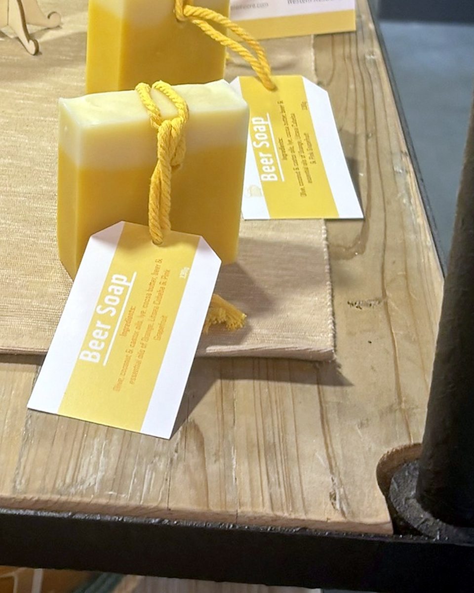 Elamoore beer soap bars tied with yellow rope, each with an ingredients tag, on a wooden shelf at Origins Market, Busselton.